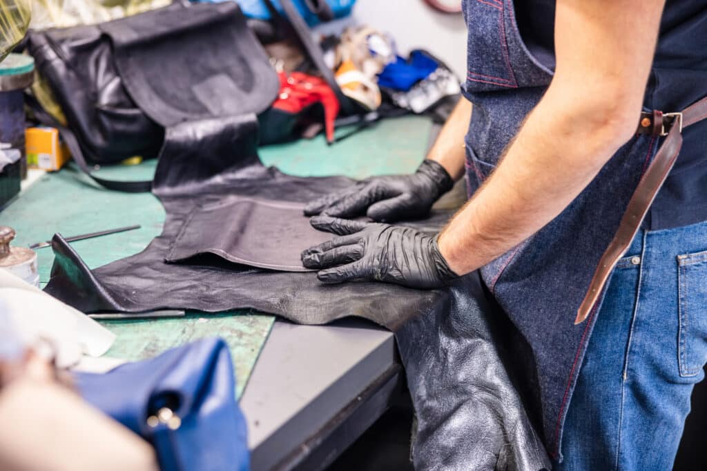 Wearing protective gloves and repairing purse with leather for replacement, crafts repair workshop